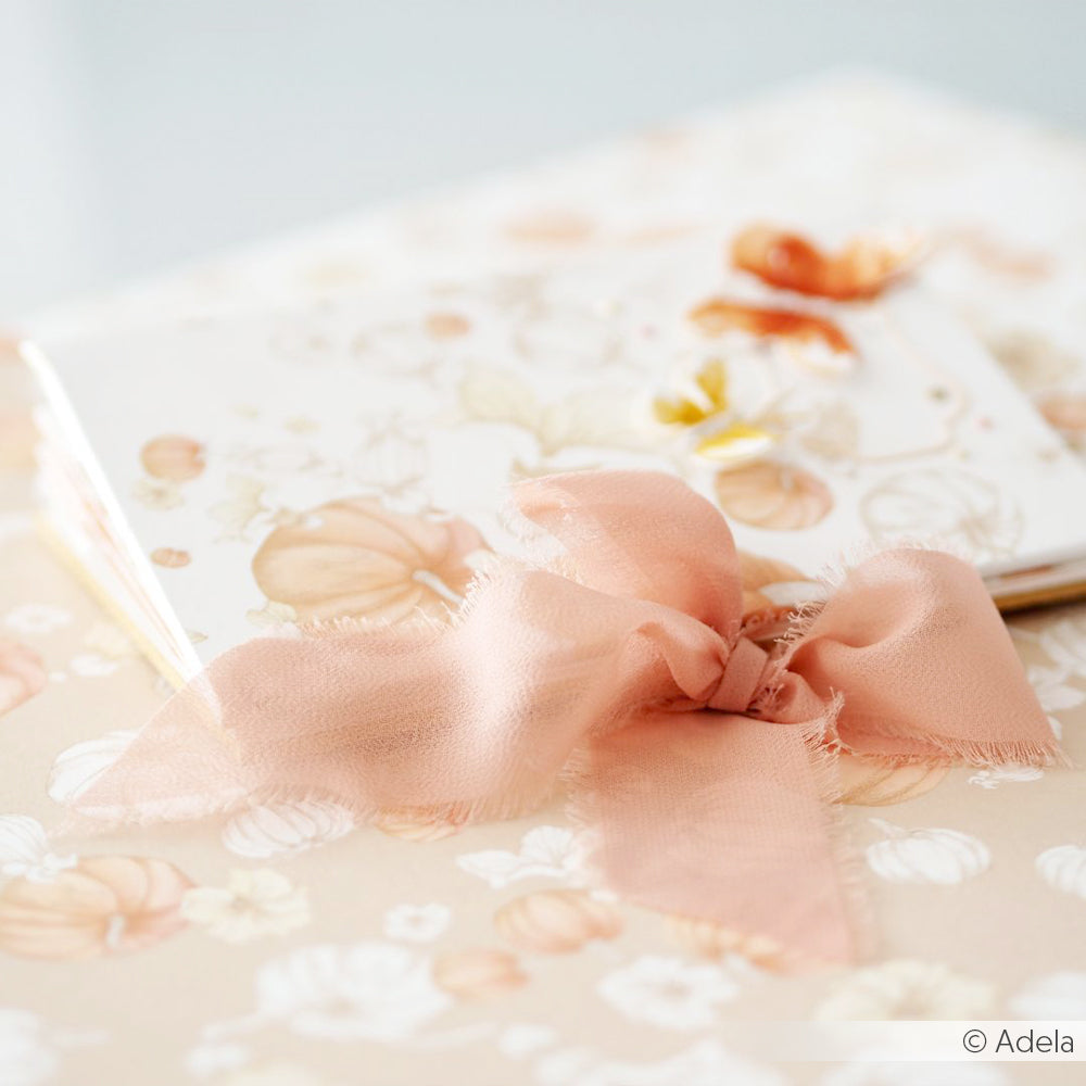 Nahaufnahme einer pastellrosa Chiffonband-Schleife von Vivant Decorations BV auf floral gemustertem Briefpapier in sanften, warmen Tönen - ideal für Bastelprojekte oder als Inspiration für Deko Ideen.