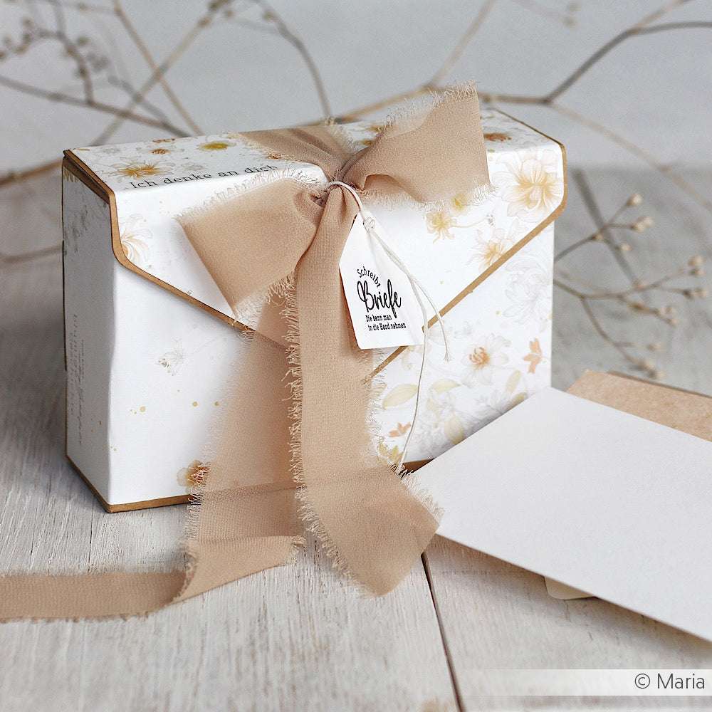Eine florale Geschenkbox von Vivant Decorations BV mit beigem Chiffonband und Anhänger, perfekt für Bastelprojekte oder Deko Ideen, steht neben Blankokarten auf einer hellen Holzfläche.