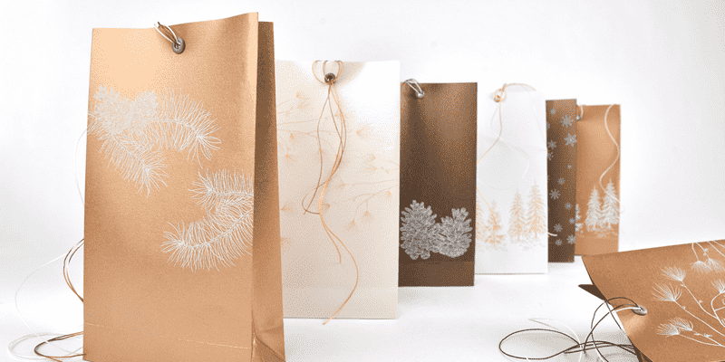 Verschiedene Geschenktüten in Weiß, Gold und Braun mit Naturmotiven, die in einer Reihe auf weißem Hintergrund angeordnet sind.