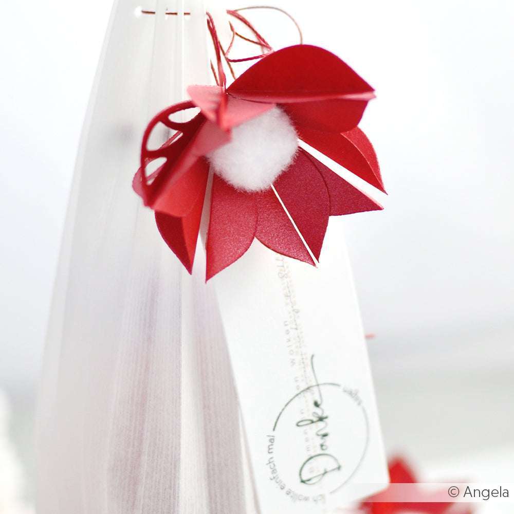 Rote und weiße Papierblume aus Glanzpapier mit einem Anhänger, der vor einem sanften, hellen Hintergrund hängt - eine typische Kreation von ☆.