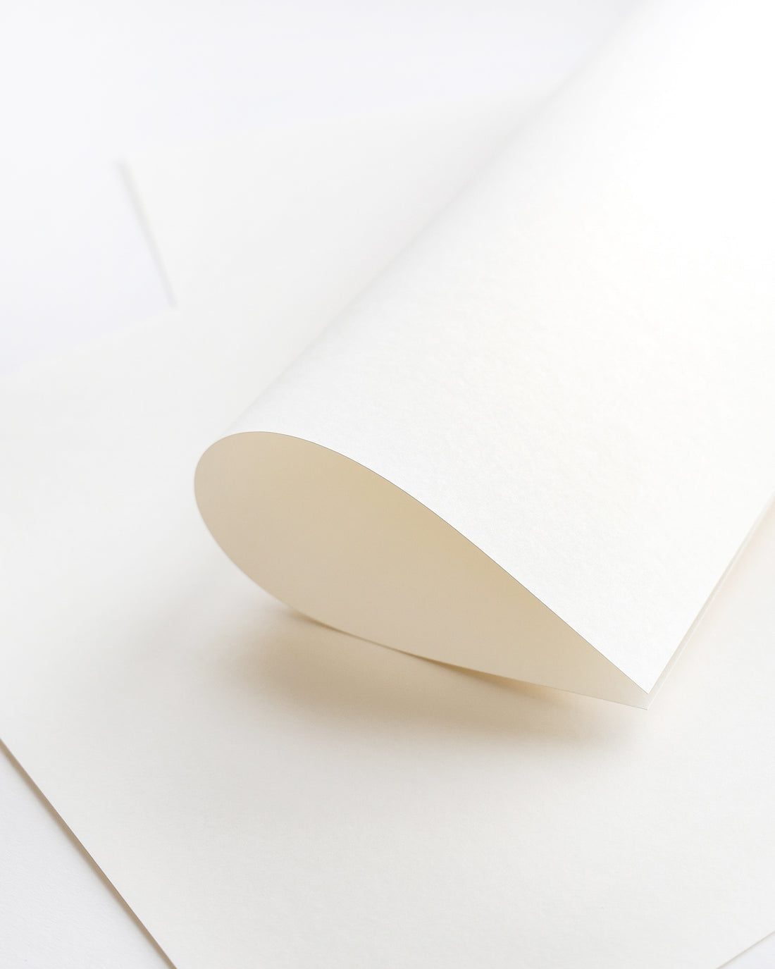 Ein einzelnes weißes Blatt Papier wird auf einer ebenen Fläche zusammengerollt, darunter liegen weitere Papierblätter.