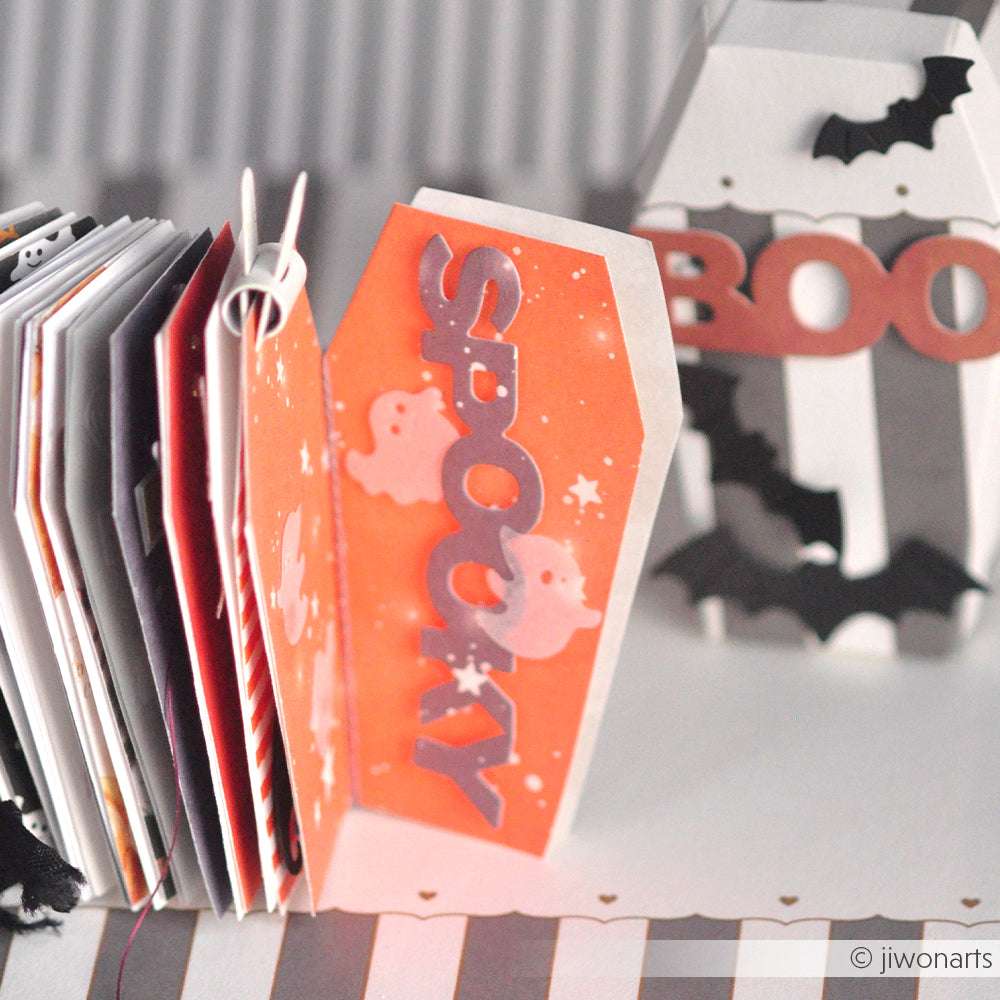 Eine kleine, sargförmige orangefarbene Spooky-Karte von Alexandra Renke steht offen neben einem Mini-Album und Halloween-Dekorationen.