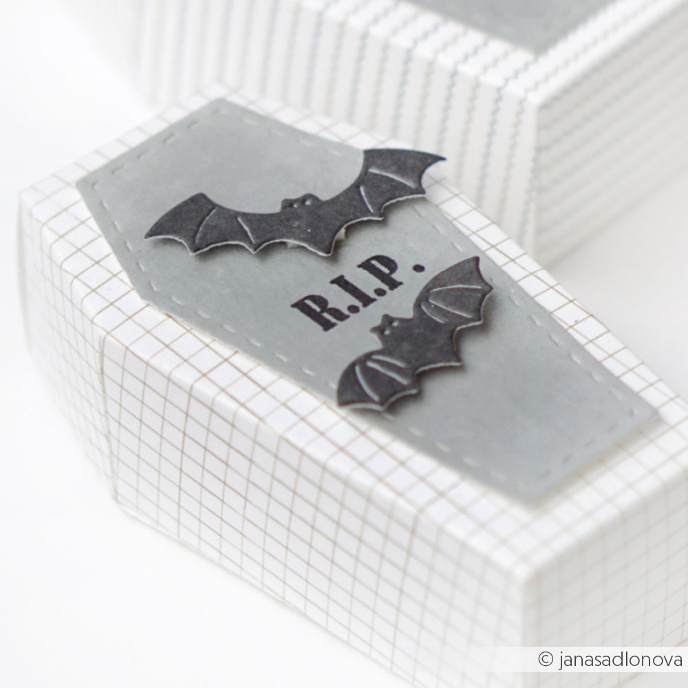 Weiße Sargschachtel mit Rasterlinien aus Alexandra Renke Designpapieren, grauem Deckel, schwarzen Fledermäusen mit Motivstanze Fledermausschwarm gestanzt und "R.I.P."-Text auf dem Deckel.