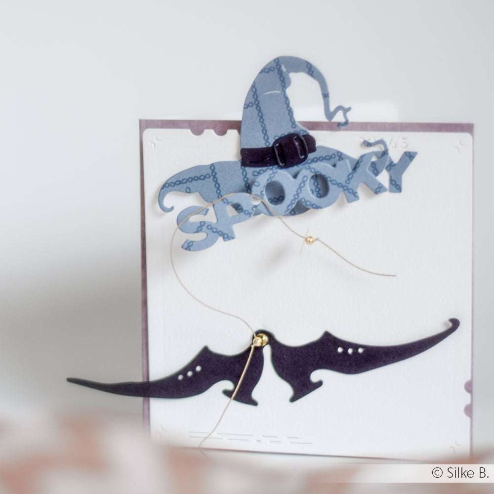 Scherenschnitte von Hexenhut und Fledermausflügeln mit Alexandra Renke Motivstanze Hexenzubehör, mit "Spooky" auf einer weißen Karte.