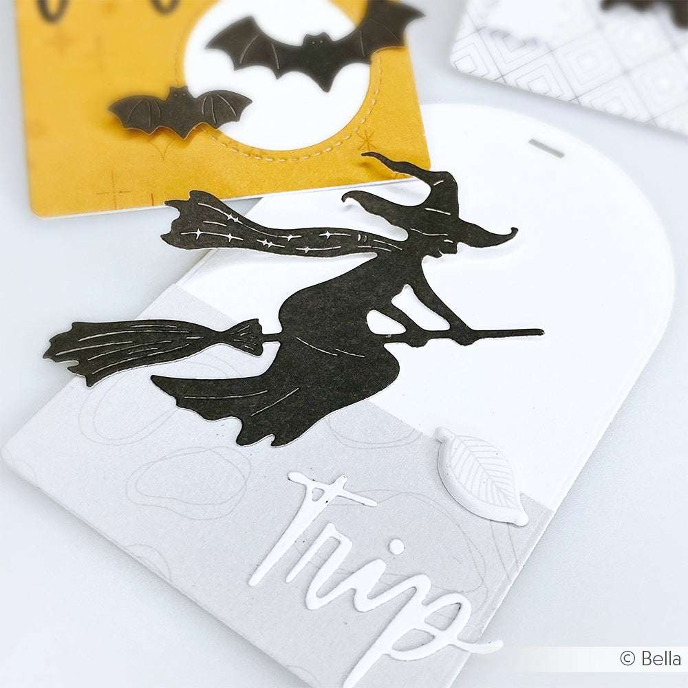 Eine schwarze Silhouette einer Hexe auf einem Besenstiel, geschnitten mit der Alexandra Renke Motivstanze Fliegende Hexe, ziert eine Karte mit dem Wort "Trip" in weißer Schrift.