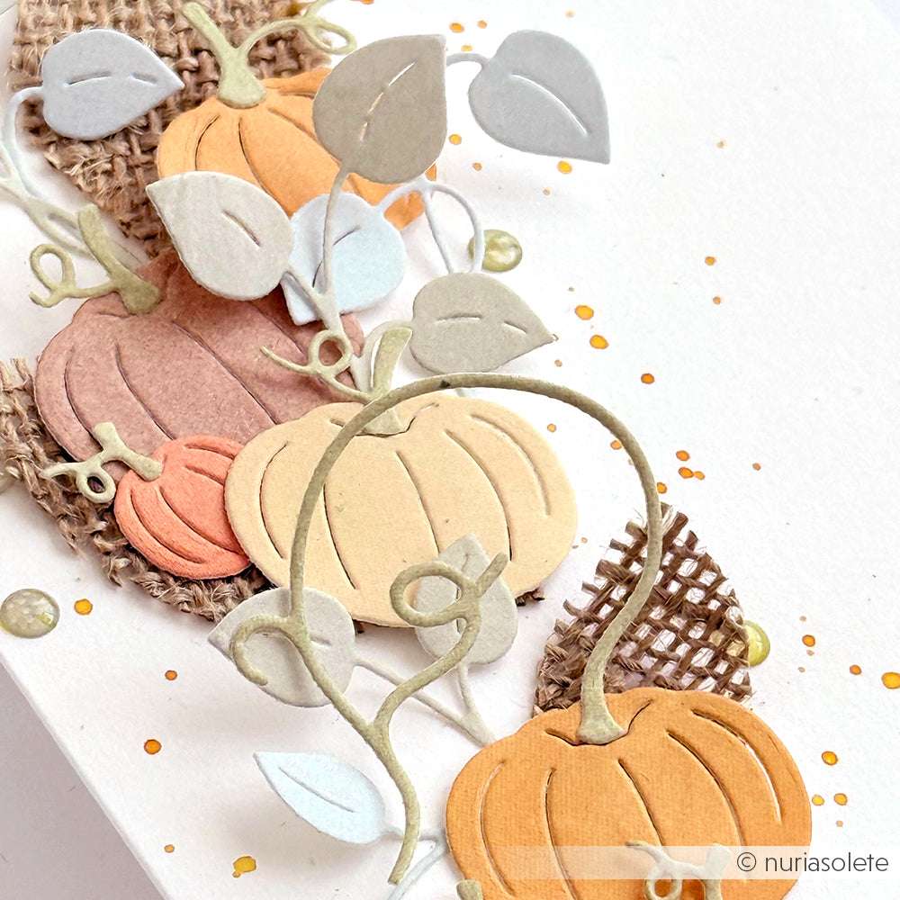 Mit Alexandra Renke Designpapieren und dem Motivstanze Kürbis Set gestaltete Papierkürbisse sind kunstvoll mit Blättern auf Sackleinen auf weißem Hintergrund mit eleganten Goldspritzern arrangiert.