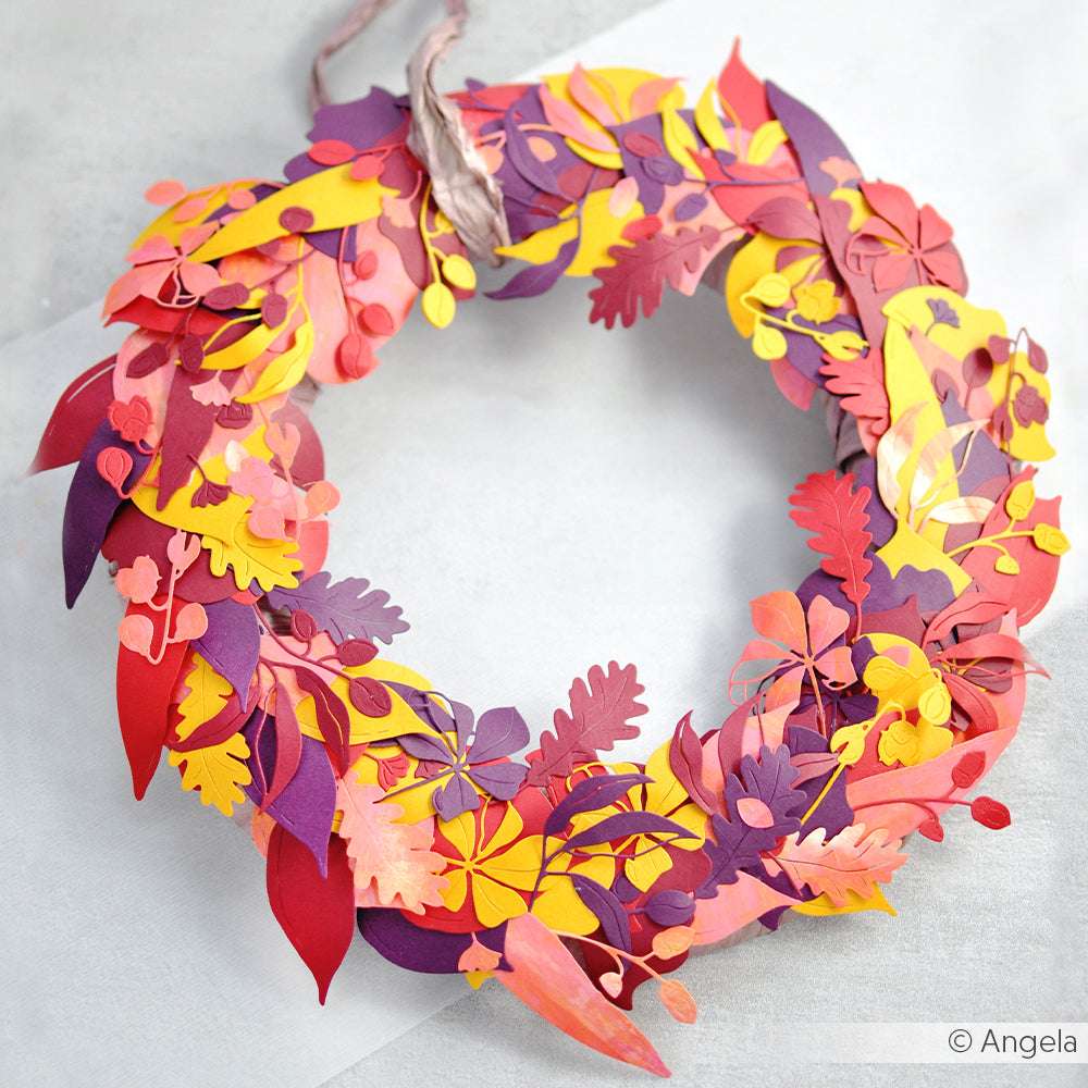Ein leuchtender Papierkranz von Alexandra Renke, gefertigt aus Designpapieren und geformt mit der "Motivstanze Walnusszweig Duo", zeigt rote, gelbe und violette Blätter und Blüten auf weißem Untergrund.