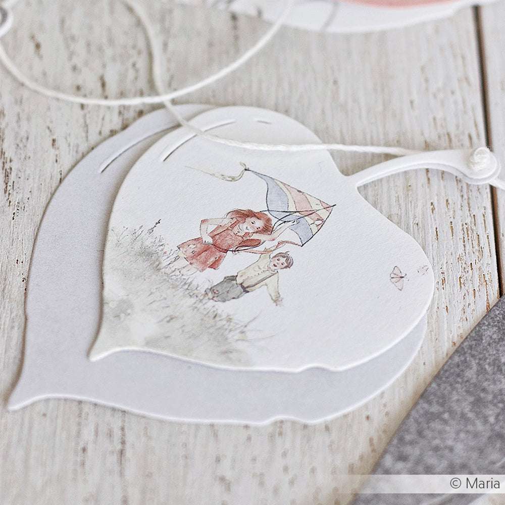 Illustration von zwei Kindern mit einem Regenschirm auf einer herzförmigen Karte, die mit Alexandra Renke Stanzen für Papier hergestellt wurde und auf einer Holzfläche ausgestellt ist.