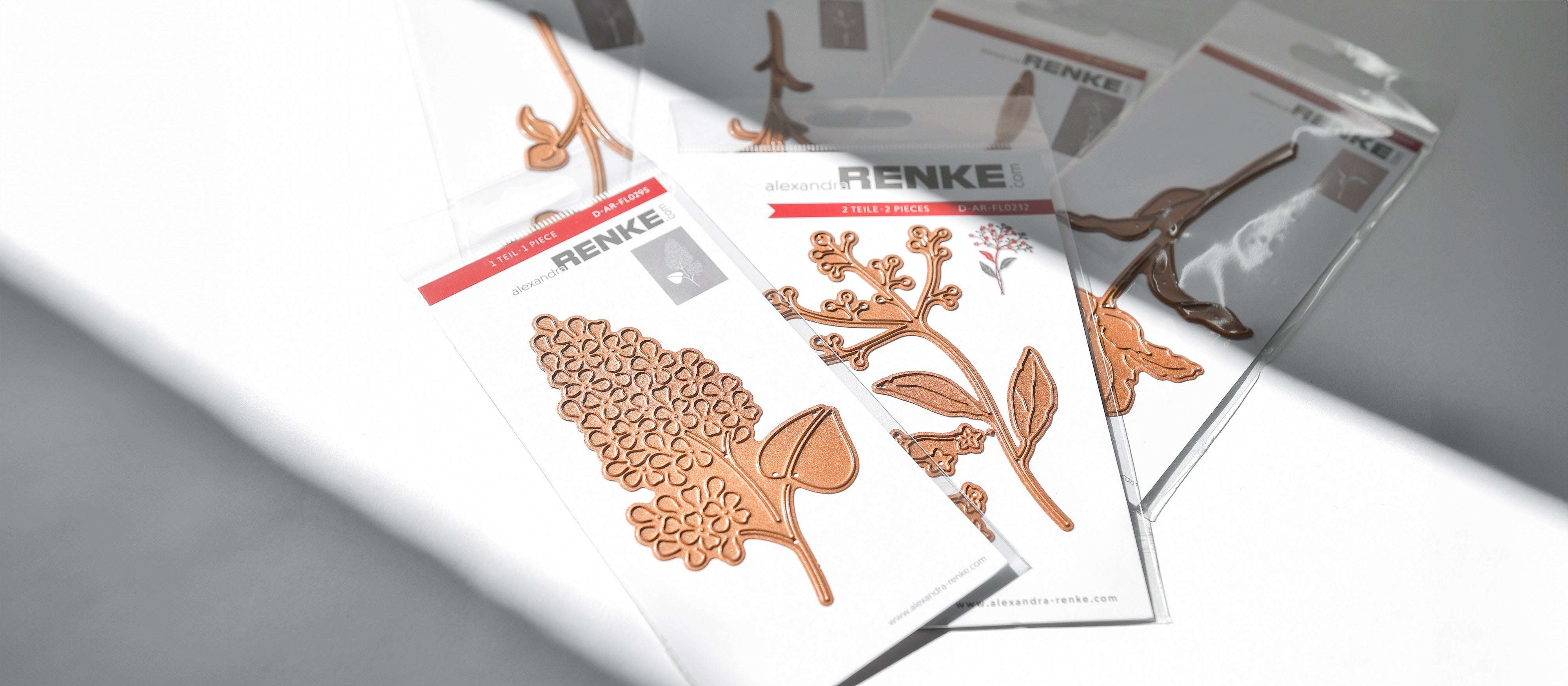 Fünf Packungen botanische Metallstanzungen auf weißem Papier, das teilweise im Sonnenlicht liegt.