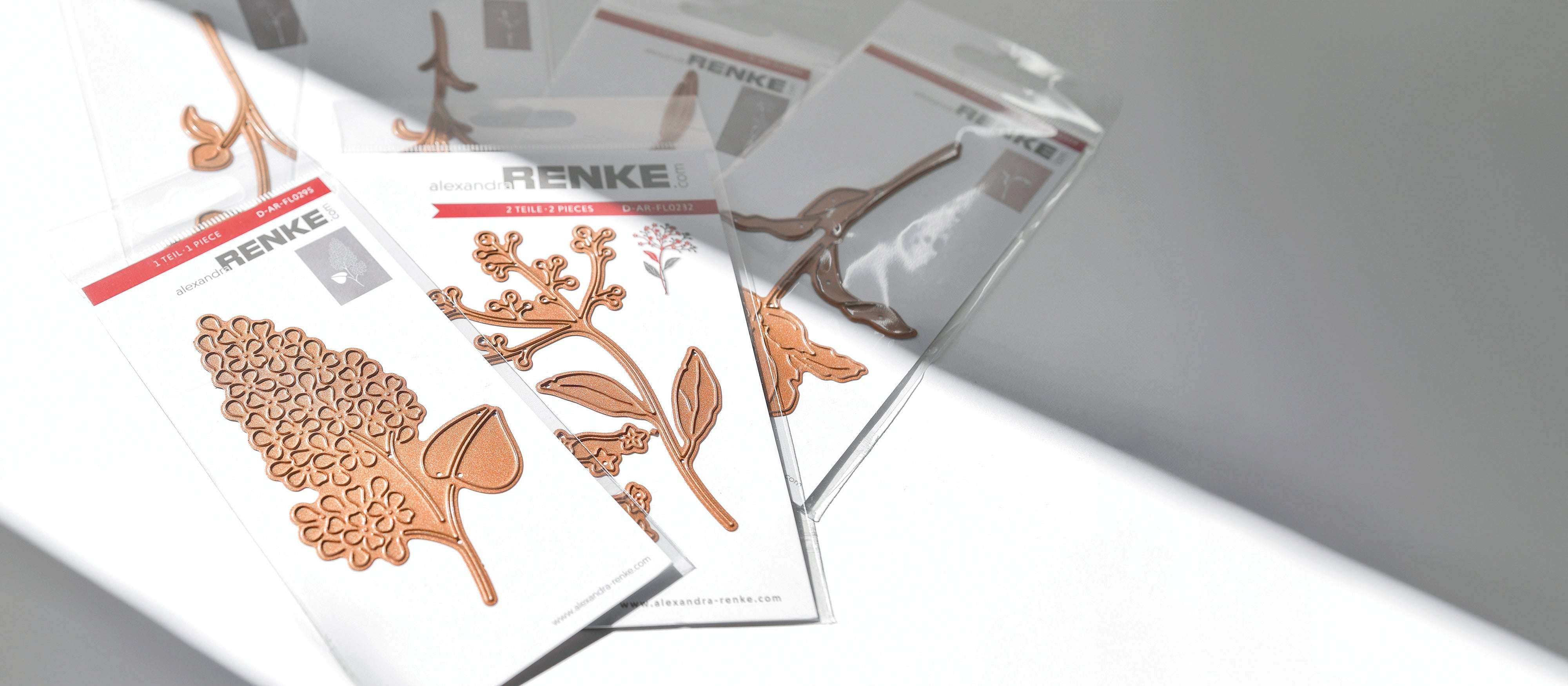 Mehrere Packungen Alexandra Renke Metallstanzteile mit floralen Motiven auf einer weißen Oberfläche.