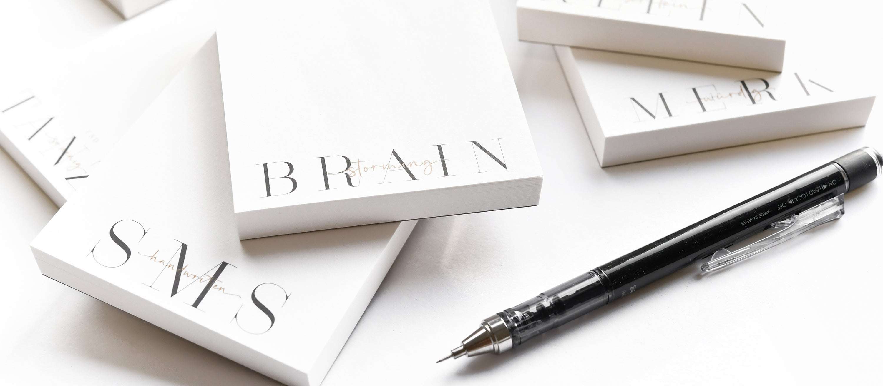 Ein schwarzer Stift und weiße Notizblöcke mit der Aufschrift BRAIN und SMS auf einer weißen Fläche.