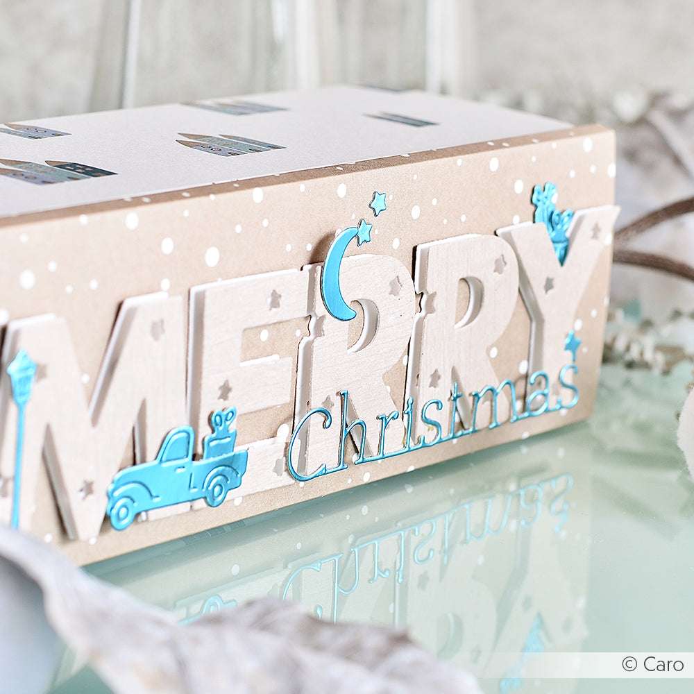 Eine dekorative ☆ Box mit "Merry Christmas" in fetten Buchstaben und aquablauen Akzenten ruht auf einer spiegelnden Oberfläche und strahlt Exklusivität aus.