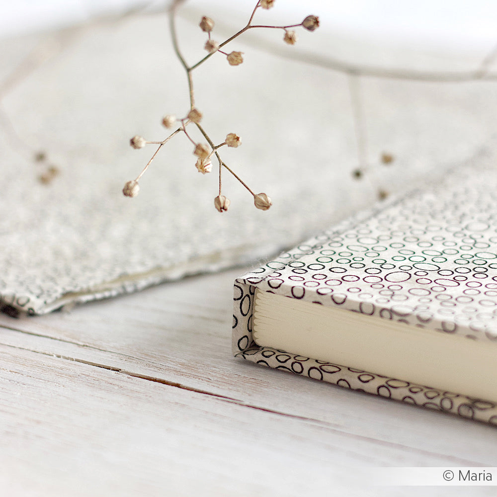 Ein ☆ gemustertes Buchblock-Notizbuch und getrocknete Blumen liegen auf einer hellen Holzoberfläche und schaffen eine weiche, minimale Ästhetik.