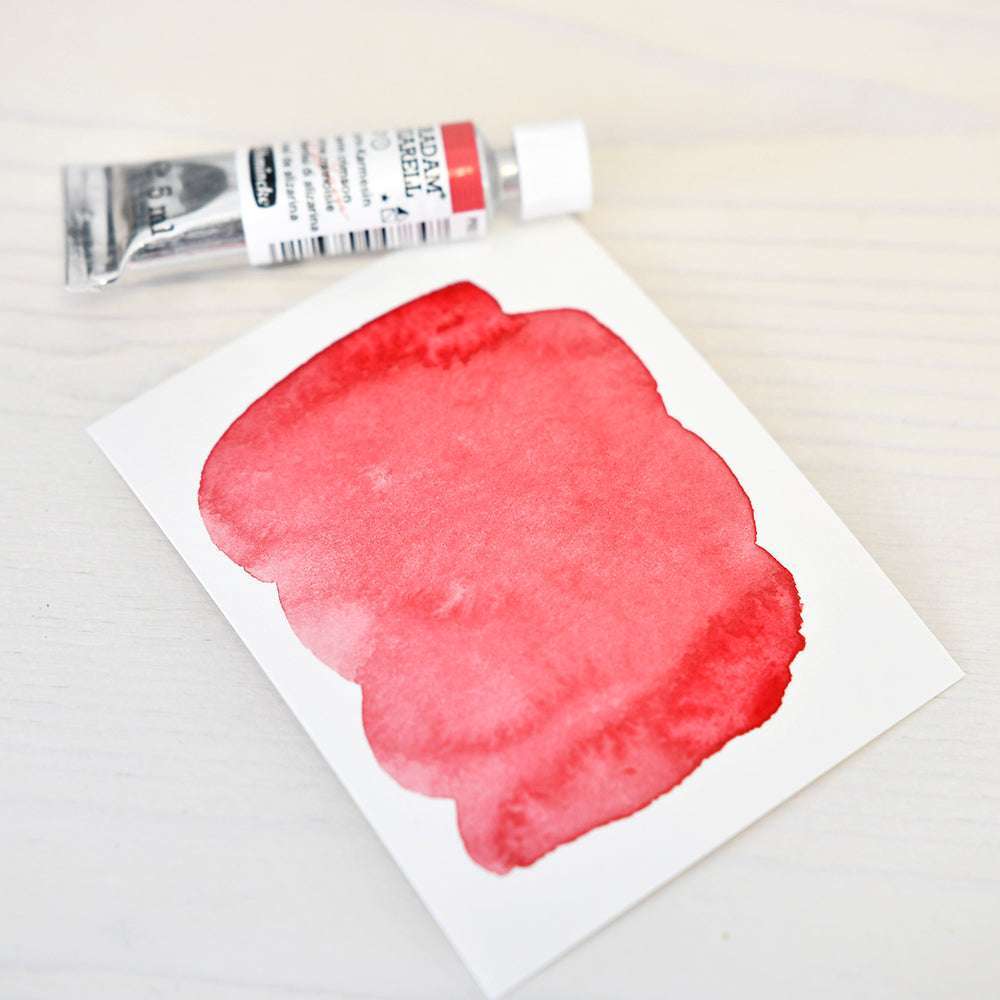 Eine Tube Schmincke-Aquarellfarbe liegt neben einem Papier, das ein rotes Muster auf hellem Grund zeigt.