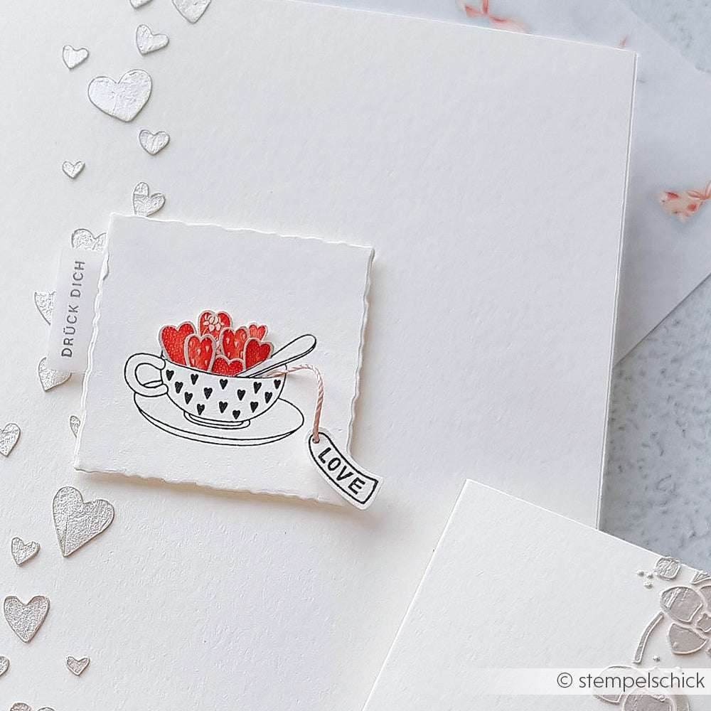 Eine Karte von Alexandra Renke mit einer Teetasse, gefüllt mit roten Herzen, Herzmustern und einem Mini Etikett Love Tea-Tag auf Weiß - ideal für charmante Akzent-Stempel- oder Holzstempel-Designs.