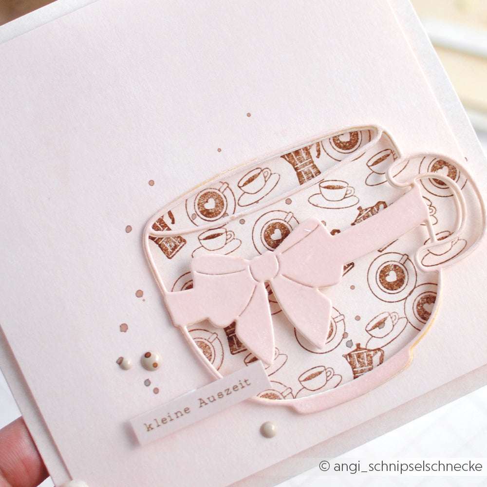 Eine hellrosa Karte von Alexandra Renke mit einer Teetasse und einer Schleife, mit Mini Kaffeetasse Herz-Motiven und dem Text "kleine Auszeit". Kombinieren Sie sie mit Holzstempel oder Akzent-Stempel für eine charmante Note.