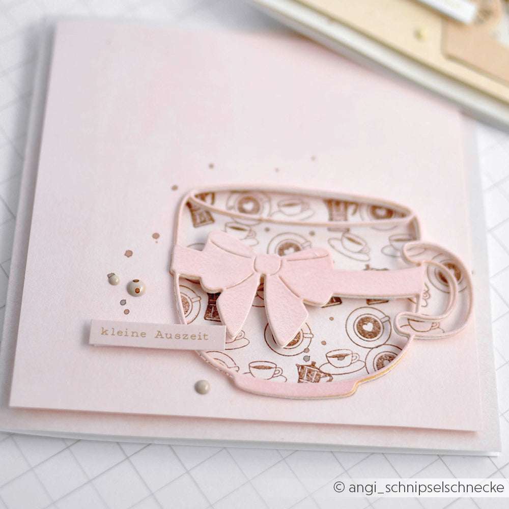 Eine pastellrosa Karte von Alexandra Renke mit einer Teetasse, einer Schleife, dem Etikett "kleine Auszeit", winzigen Perlenakzenten und dem Charme eines Mini Kaffeetasse Stempels.