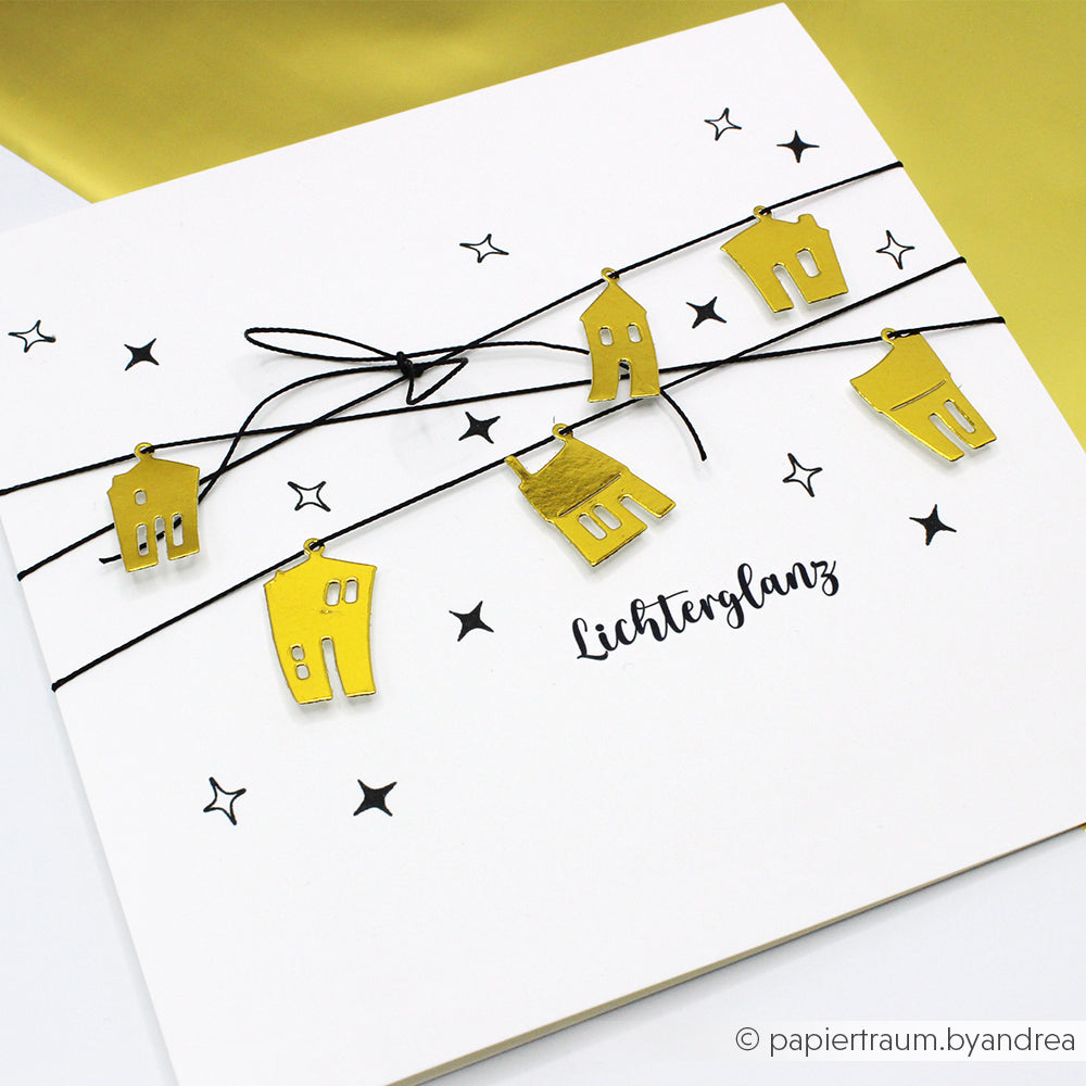 Eine Karte von Alexandra Renke mit goldenen Anhängern in Form eines Hauses auf einer schwarzen Schnur, Sternen und "Lichterglanz" in Schrift - ideal, um Ihren Lieblings-Akzent-Stempel zu präsentieren oder mit einem einzigartigen Holzstempel zu kombinieren, der eine besondere Note erhält.