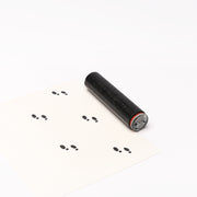 Ein schwarzer Alexandra Renke Stempel Roller druckt Mini Fußspuren als kleine schwarze Abdrücke auf ein weißes Blatt Papier.