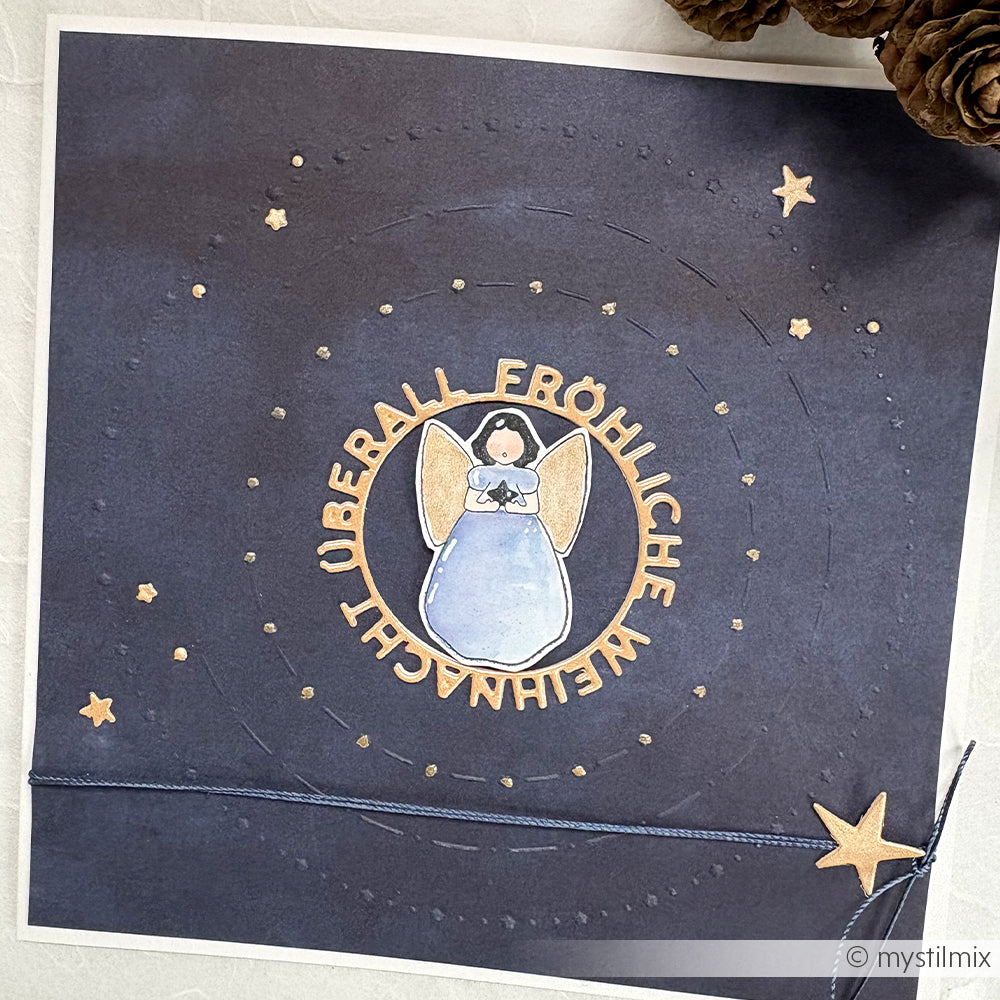 Eine handgefertigte Karte von Alexandra Renke zeigt einen Engel in der Mitte und "Fröhliche Weihnachten überall" in einem Kreis, der mit Holzstempeln und Stempelkissen verziert ist.