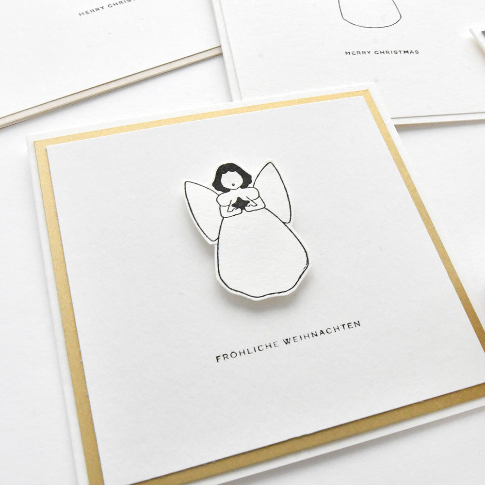 Eine Weihnachtskarte von Alexandra Renke mit einem schlichten Engelmotiv aus Holzstempeln und dem Schriftzug "Fröhliche Weihnachten" darunter.