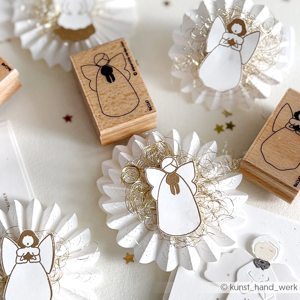 Alexandra Renke Papierengel und Holzstempel, darunter ein Stiller Engel Motivstempel, sind auf einer weißen Fläche mit goldenen Akzenten angeordnet.