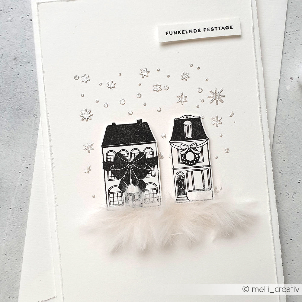 Die minimalistische Weihnachtskarte von Alexandra Renke zeigt zwei illustrierte Häuser, Sterne, einen Federsockel und den Schriftzug FUNKELNDE FESTTAGE für festliche Grüße in einer gemütlichen Schleifenhaus-Szene.