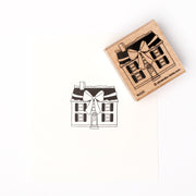 Ein hochwertiger Holzstempel von Alexandra Renke zeigt ein detailreiches Haus mit großer Schleife über der Tür und hinterlässt einen klaren Abdruck auf weißem Papier.