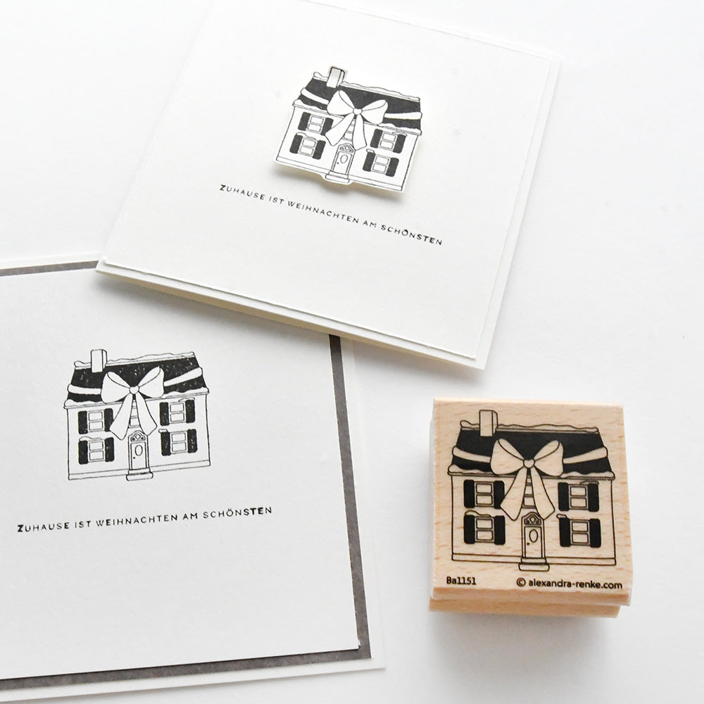 Quadratische Karte und Briefmarke von Alexandra Renke mit einer schwarz-weißen Haus-Illustration und dem deutschen Text "Zuhause ist Weihnachten am schönsten." Einzigartiges Design auf einem hochwertigen Holzstempel.
