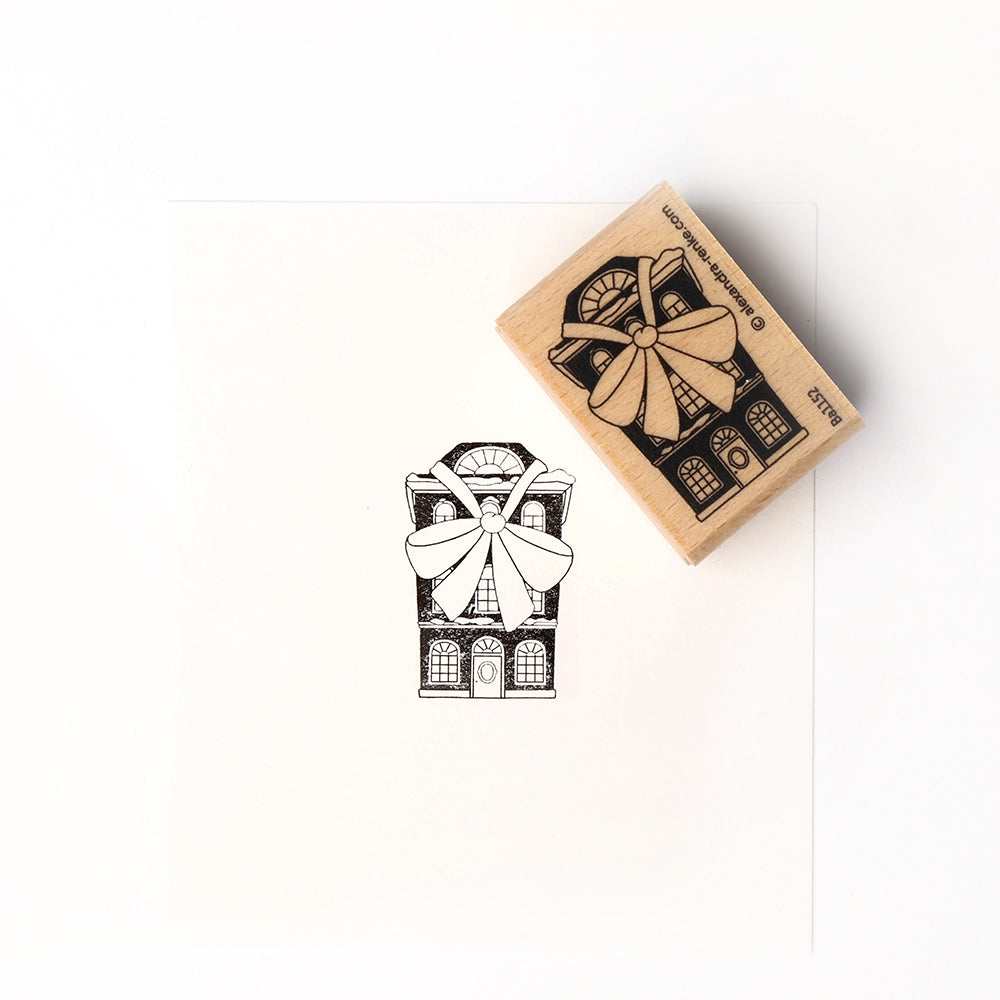 Neben dem fein geschnitzten Stempel ist ein gestempeltes schwarz-weißes Haus mit einer großen Schleife zu sehen, das mit dem hochwertigen Holz Holzstempel von Alexandra Renke hergestellt wurde.