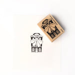 Neben dem fein geschnitzten Stempel ist ein gestempeltes schwarz-weißes Haus mit einer großen Schleife zu sehen, das mit dem hochwertigen Holz Holzstempel von Alexandra Renke hergestellt wurde.