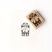 Neben dem fein geschnitzten Stempel ist ein gestempeltes schwarz-weißes Haus mit einer großen Schleife zu sehen, das mit dem hochwertigen Holz Holzstempel von Alexandra Renke hergestellt wurde.