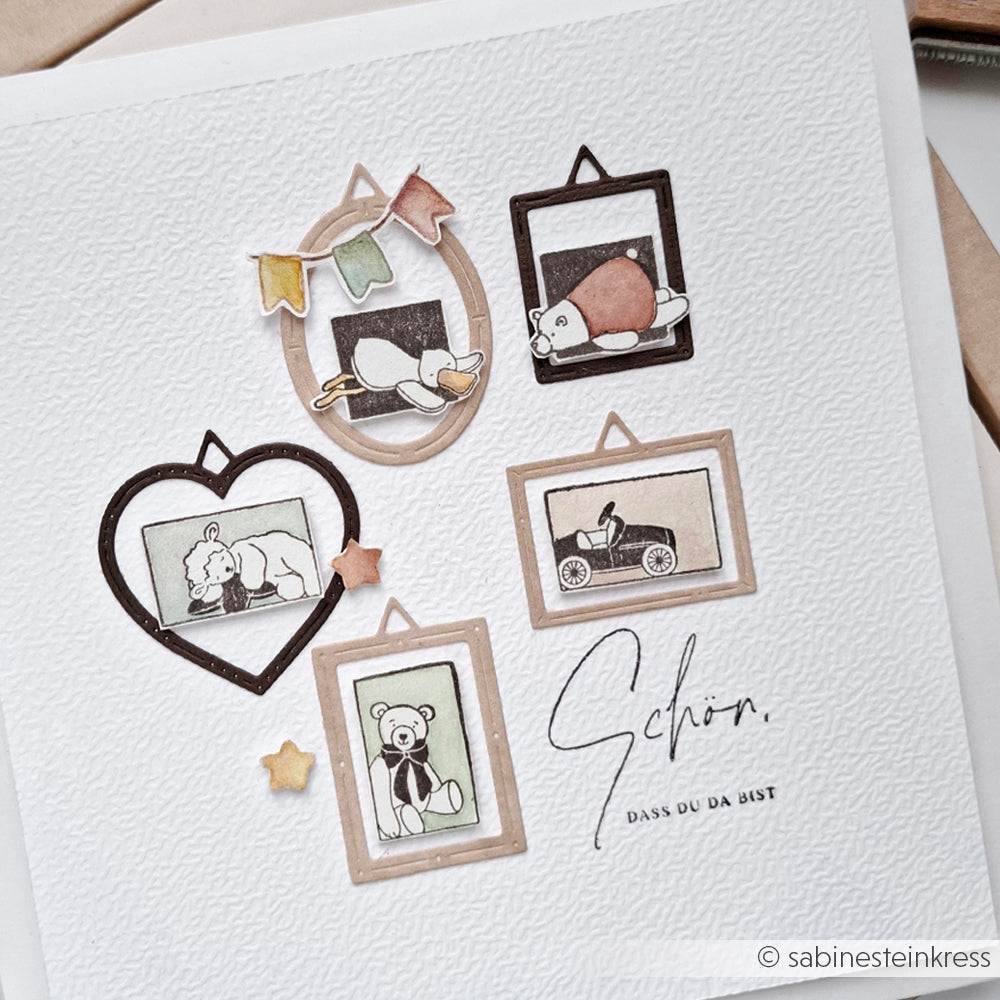 Gerahmte Illustrationen von niedlichen Tieren, einem Teddybär und einem Spielzeugauto sind auf strukturiertes weißes Papier mit dekorativen Sternen gedruckt und zeigen charmante Details, die von Holzstempel-Designs von Alexandra Renke inspiriert sind.