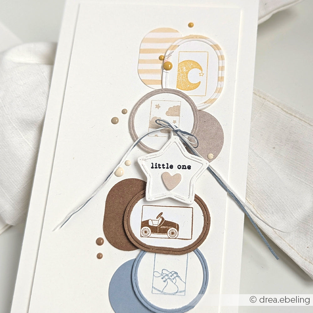Eine handgefertigte Karte mit geschichteten Kreisen, einem Stempelmotiv zum Thema Baby und einem Sternanhänger mit der Aufschrift "Kleines", der mit einer Schleife gebunden wird - hergestellt mit dem charmanten Alexandra Renke Holzstempel für zusätzliche Details.