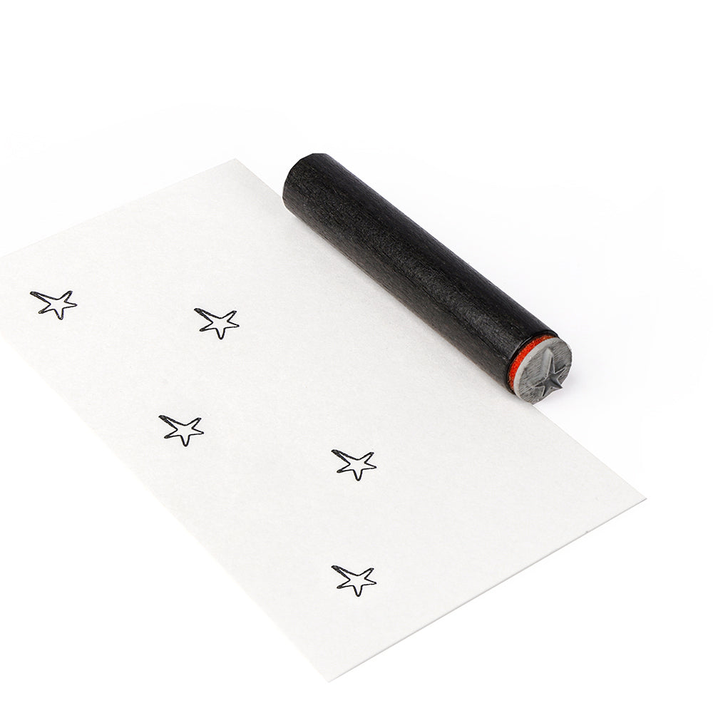 Ein schwarzer sternförmiger Holzstempel von Alexandra Renke ruht auf einem Papier, das mit gestempelten schwarzen Sternen verziert ist, wodurch ein charmanter Mini Stern Outline-Effekt entsteht.