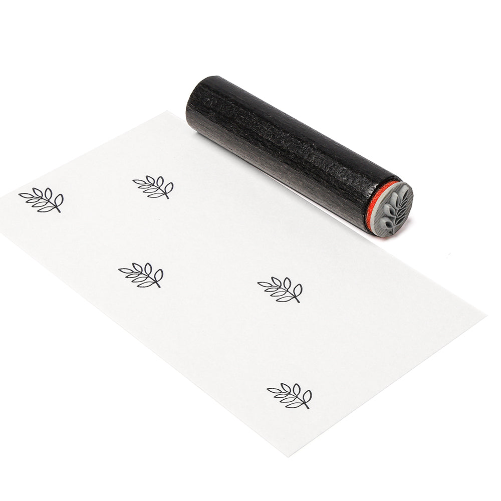 Ein schwarzer Holzstempel aus Gummi von Alexandra Renke und Papier mit einem sich wiederholenden gestempelten Blattmotiv, das das Mini Palmzweig Motiv als eleganten Akzentstempel enthält.