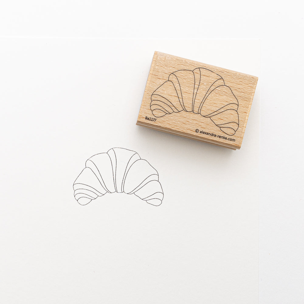 Ein hölzerner Alexandra Renke Stickvorlagen-Stempel mit einem Croissant-Motiv, abgebildet in Tinte auf weißem Papier gestempelt.