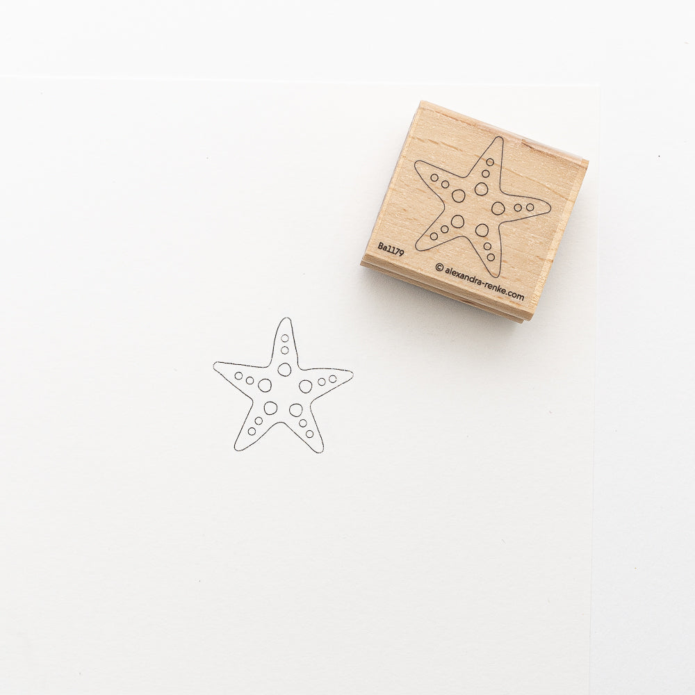 Der Holzstempel von Alexandra Renke zeigt ein Seesternmotiv und ist neben dem gestempelten Umriss auf weißem Papier abgebildet.