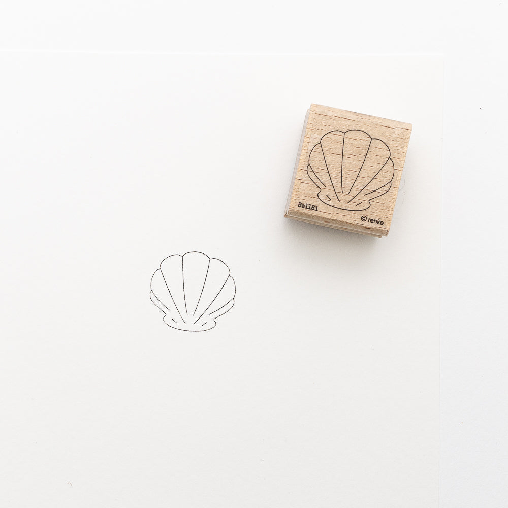 Ein Holzstempel von Alexandra Renke mit Muschelmotiv wird neben seinem scharfen Abdruck mit schwarzer Tinte ausgestellt, ideal für Stickprojekte oder als Teil von individuellen Geschenken.