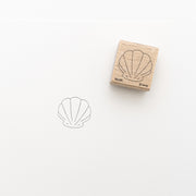 Ein Holzstempel von Alexandra Renke mit Muschelmotiv wird neben seinem scharfen Abdruck mit schwarzer Tinte ausgestellt, ideal für Stickprojekte oder als Teil von individuellen Geschenken.