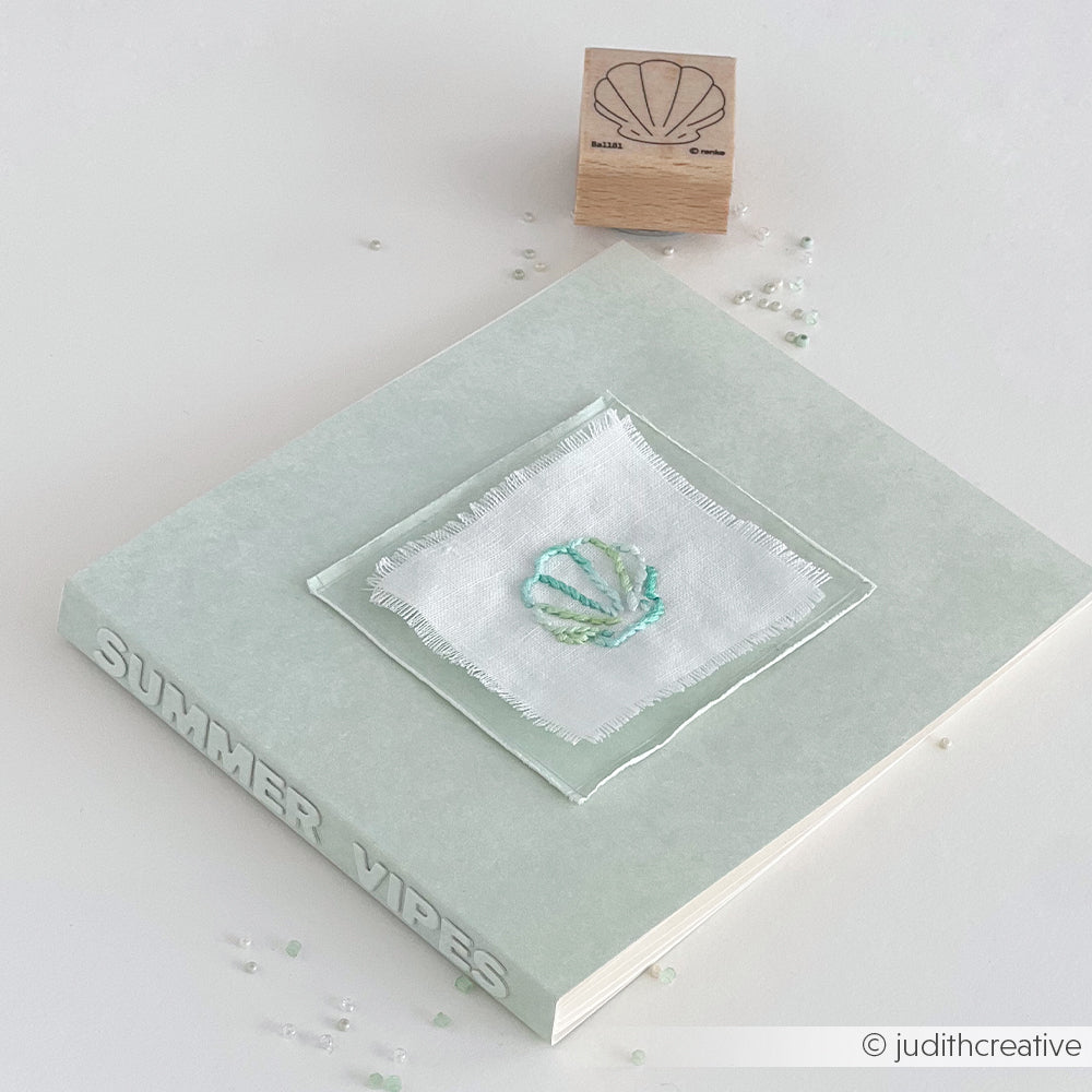 Ein hellgrünes Buch von Alexandra Renke mit dem Titel SUMMER VIBES, mit einem Muschelaufnäher und einem passenden Stempel - die perfekte Inspiration für Stickprojekte oder zum Testen der Stempelfarbe für Stoff.