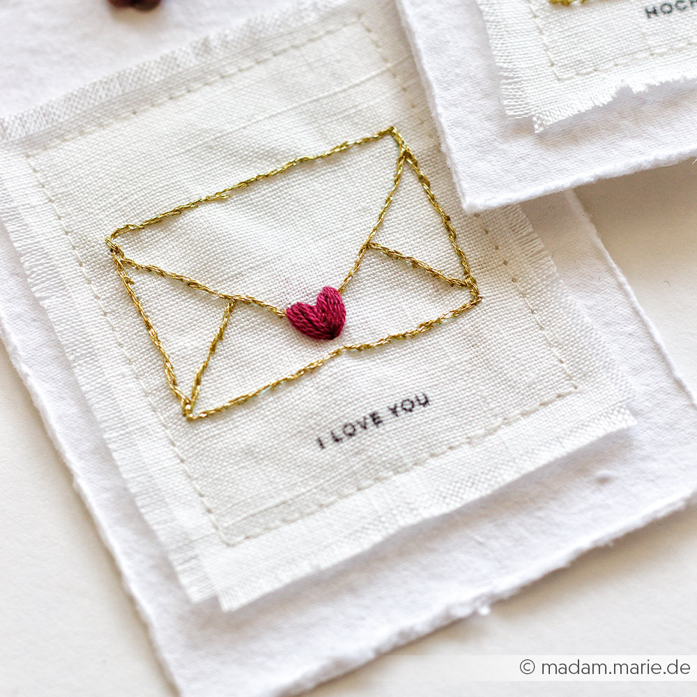 Ein Stoffaufnäher von Alexandra Renke mit einem goldgestickten Umschlag und einem roten Herz mit "I LOVE YOU" darunter - ideal für einzigartige Geschenke oder um Ihren Stickprojekten Charme zu verleihen.