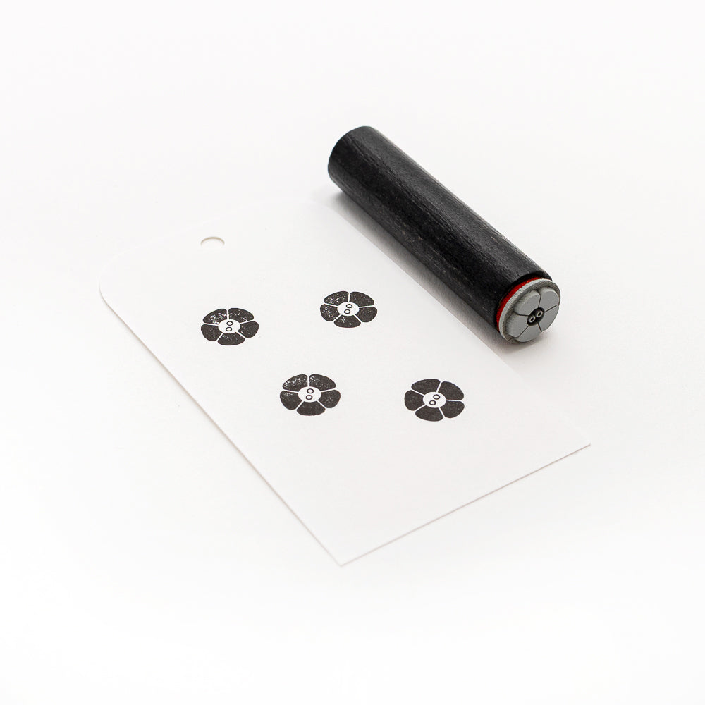 Ein schwarzer Holzstempel und eine weiße Karte, die mit vier schwarzen Blumenmustern mit der Nummer 8 bestempelt sind - perfekt für Papierprojekte oder um Ihre Bastelarbeiten mit einem charmanten Alexandra Renke Stempel Mini Blumenknopf zu versehen.