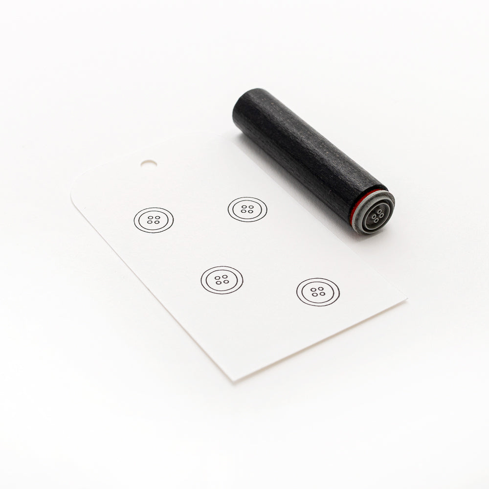 Ein schwarzer Alexandra Renke Holzstempel und eine weiße Karte mit fünf gestempelten Knopfmotiven, jeweils mit vier Löchern. Ideal als Mini Knopf Stempel oder für Anfänger.