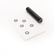 Ein schwarzer zylindrischer Alexandra Renke Mini Knopf Stempel wird neben eine weiße Karte gelegt, auf der sechs kleine schwarze Zielsymbole abgebildet sind.