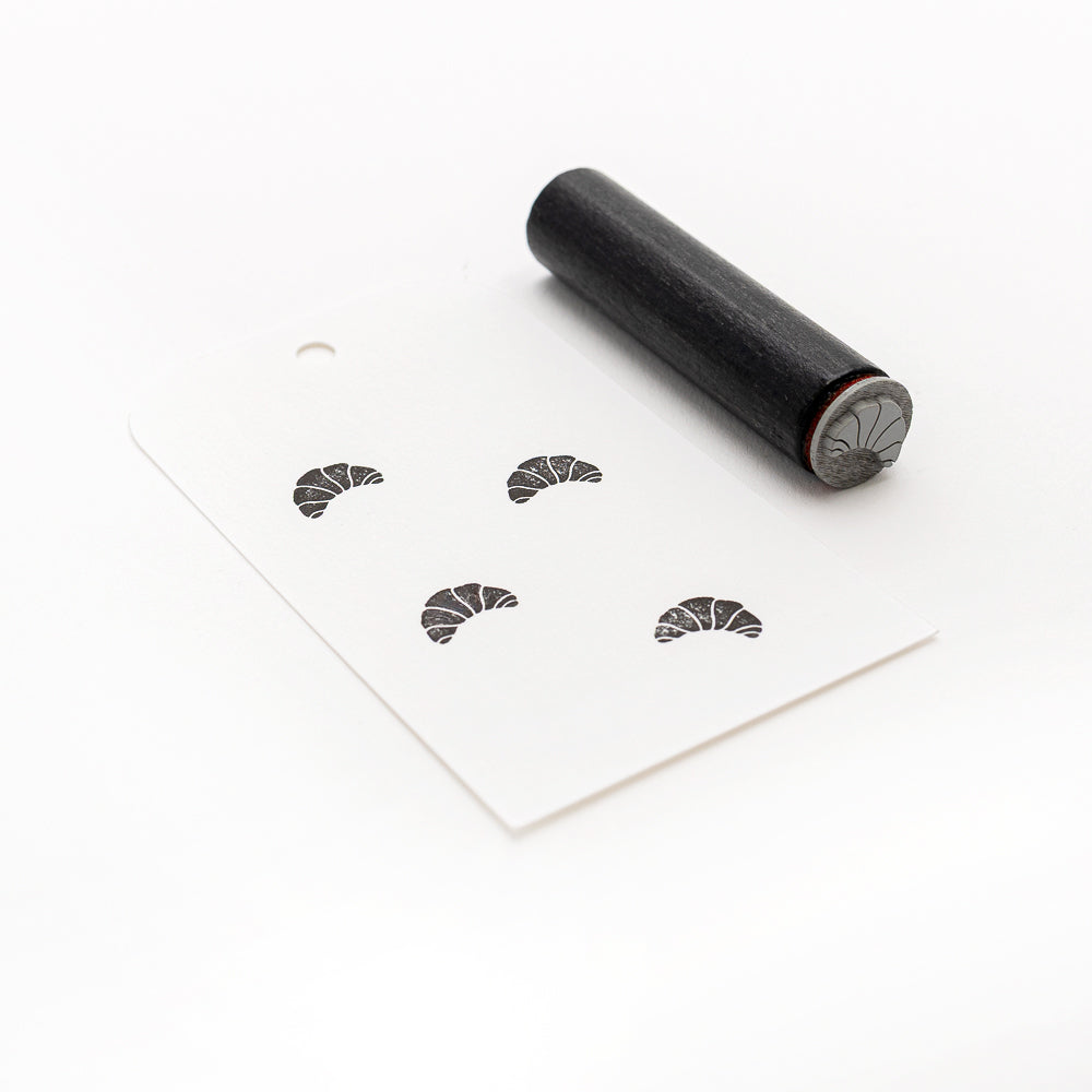 Alexandra Renke Akzent-Stempel aus schwarzem Gummi und weißer Anhänger mit mehreren gestempelten Fächerformen, die einem Mini-Croissant-Muster ähneln, sind auf weißem Hintergrund abgebildet.