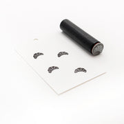 Alexandra Renke Akzent-Stempel aus schwarzem Gummi und weißer Anhänger mit mehreren gestempelten Fächerformen, die einem Mini-Croissant-Muster ähneln, sind auf weißem Hintergrund abgebildet.