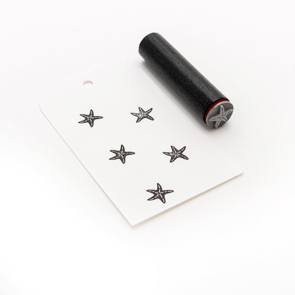 Der Alexandra Renke Akzent-Stempel Mini Seestern zaubert fünf Seesterne auf ein knackig weißes Papierschild, die alle mit einem handgeschnitzten Stempel auf einem sauberen weißen Hintergrund hergestellt wurden.