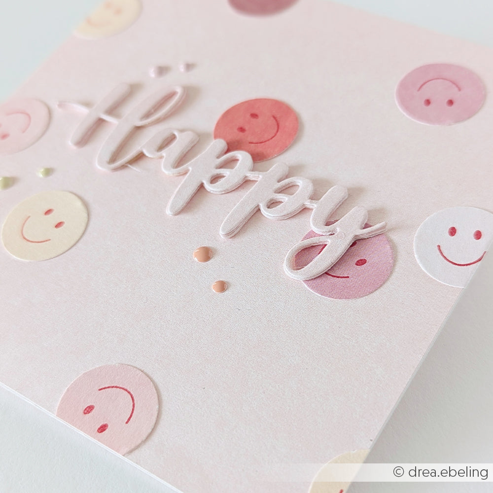 Eine Karte mit pastellfarbenen Smileys und dem Wort „Happy“ in erhabener Schrift auf hellem Hintergrund, die wunderbar an Motive erinnert, die mit Stempelgummi oder Holzstempeln und Ihrem Lieblingsstempelkissen gestaltet wurden.