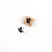 Ein Holzstempel und sein Abdruck, der die Silhouette eines Engels zeigt, der ein Herz bläst, mit detailreichen Motiven.
